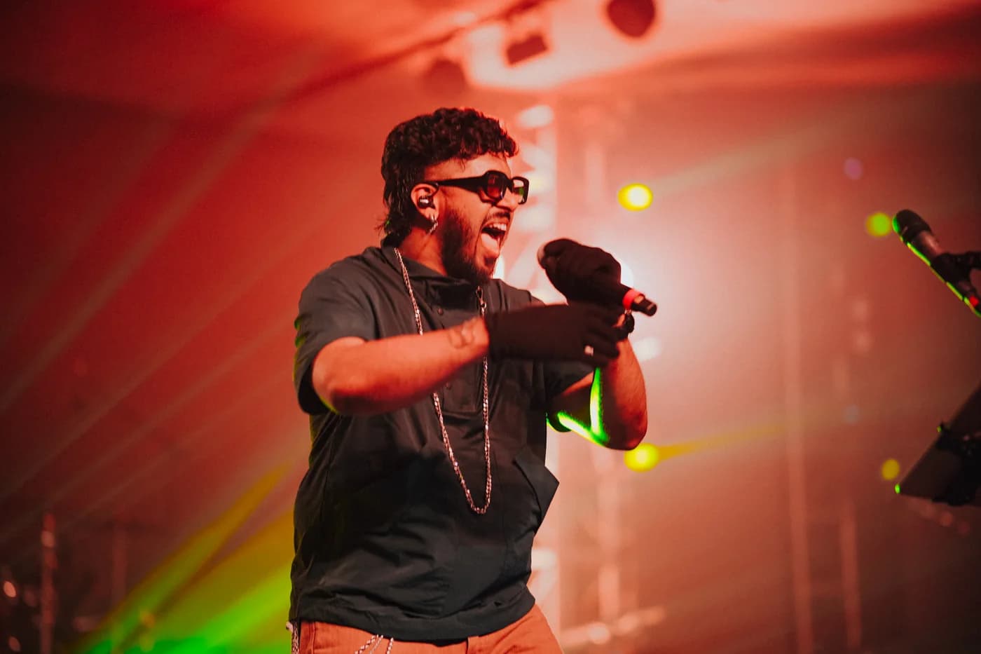 Faisal Razi singing into a microphone beneath warm red concert lights